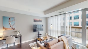A modern living room with a large window, a flat-screen TV, and a dining area with a table and chairs. - Modern Central 1-BR Condo in DT Toronto (Toronto)