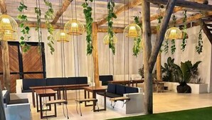 An indoor space with a wooden ceiling, hanging plants, and a seating area with tables and chairs. - Hotel All In One  (Armenia)