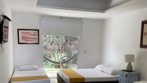 A hotel room with two beds, a small table with a lamp, and a window with a view of greenery. - Hotel All In One  (Armenia)