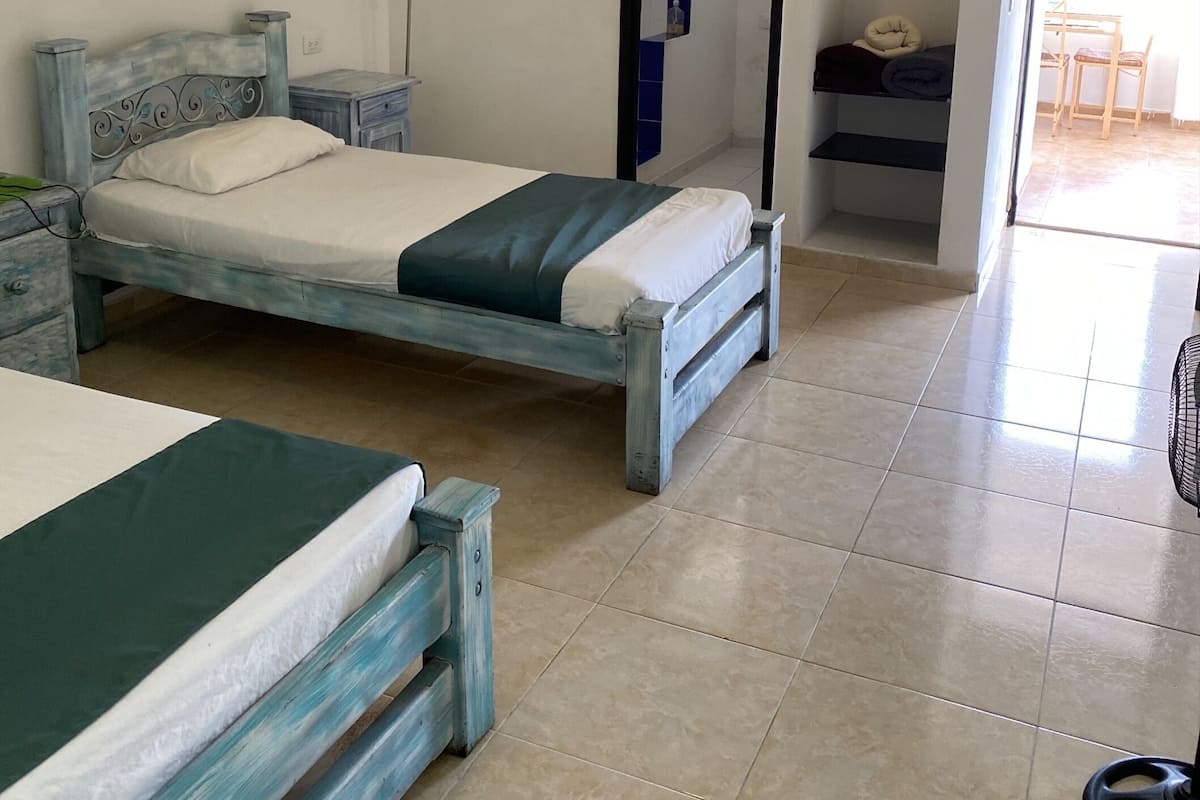 Un dormitorio con cama, mesita de noche, lámpara de pared y un baño visible a través de una puerta abierta.