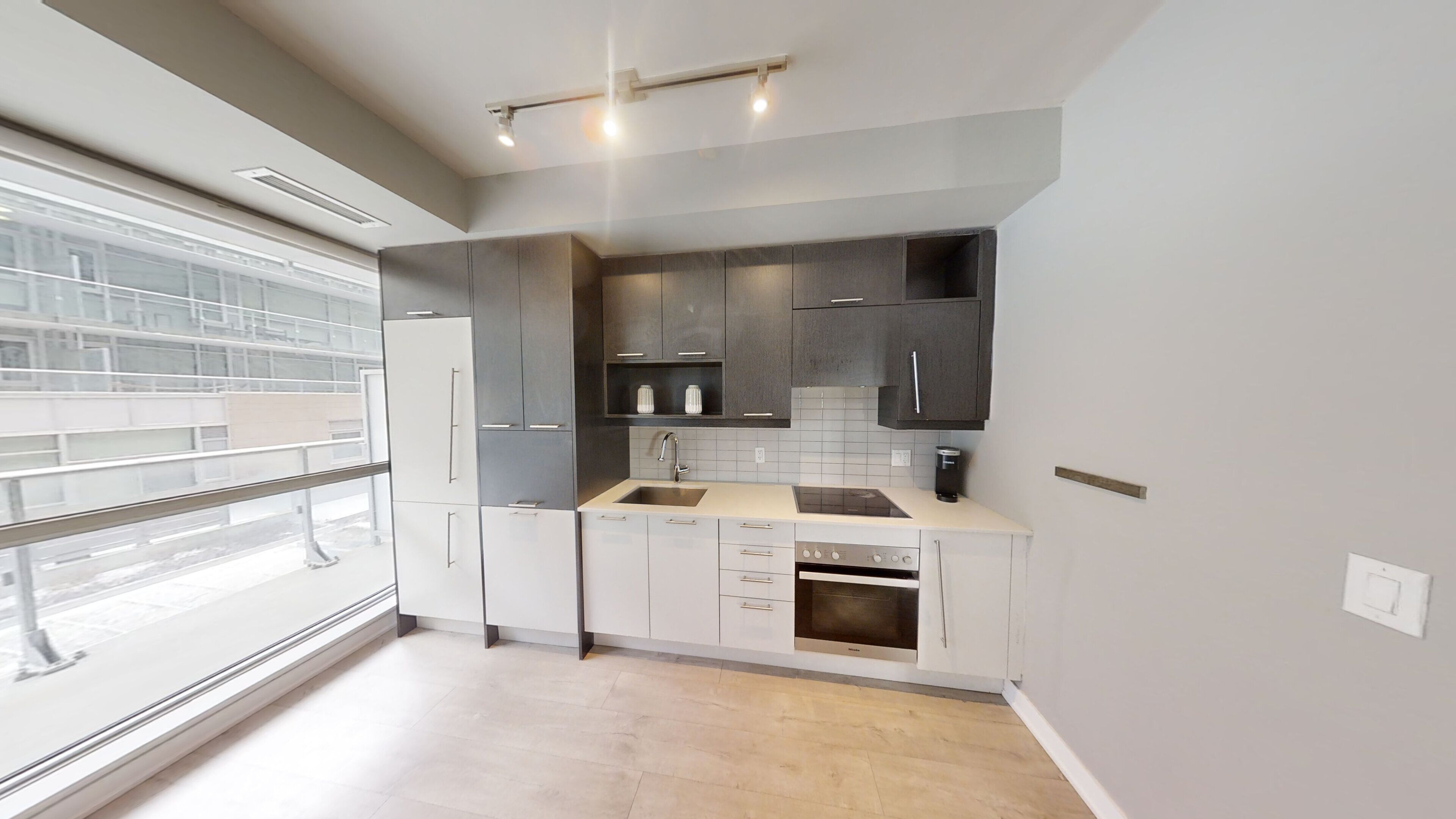 A modern kitchen with a large window, white cabinets, and a built-in oven.