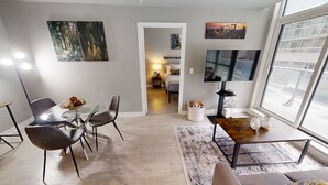 A modern living room with a dining area, large windows, and artwork on the walls. - Modern Central 1+1-BR Condo in DT Toronto (Toronto)