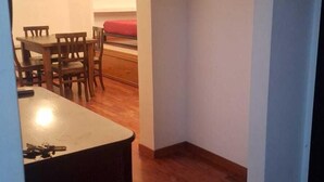 Une cuisine avec un plancher en bois, un coin repas avec des chaises et une table, et un couloir avec une porte.
