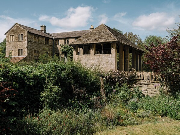 A stone building with a large window and a chimney, surrounded by dense vegetation.