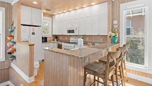 A kitchen with wooden paneling, white cabinets, a central island with bar stools, and a window with a view. - Carillon Beach - Grits Carlton by PHG (Panama City Beach)