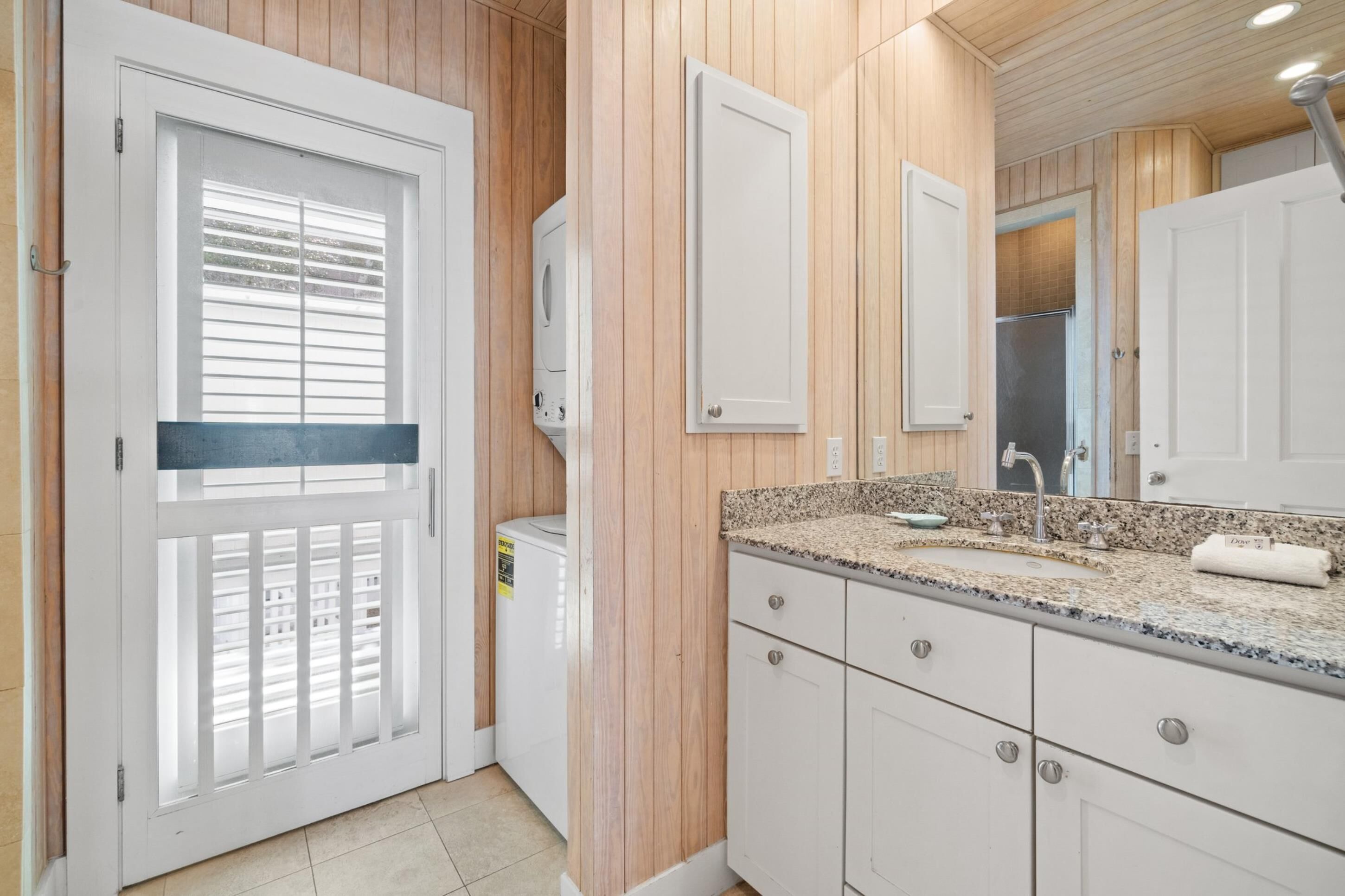 Un baño moderno con paneles de madera, un lavabo blanco sobre encimera de granito y un espejo grande.