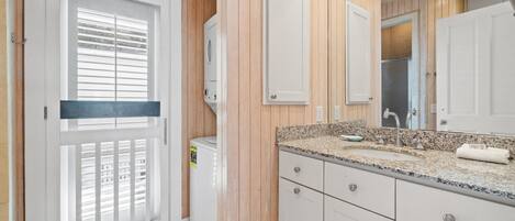 Un baño moderno con paneles de madera, un lavabo blanco sobre encimera de granito y un espejo grande.