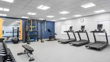Un gimnasio con cintas de correr, mancuernas, una estructura para sentadillas y una bicicleta estática.
