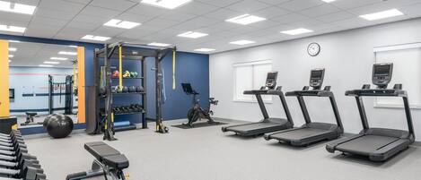 Une salle de sport équipée de tapis de course, d’haltères, d’un support à squats et d’un vélo d’appartement.