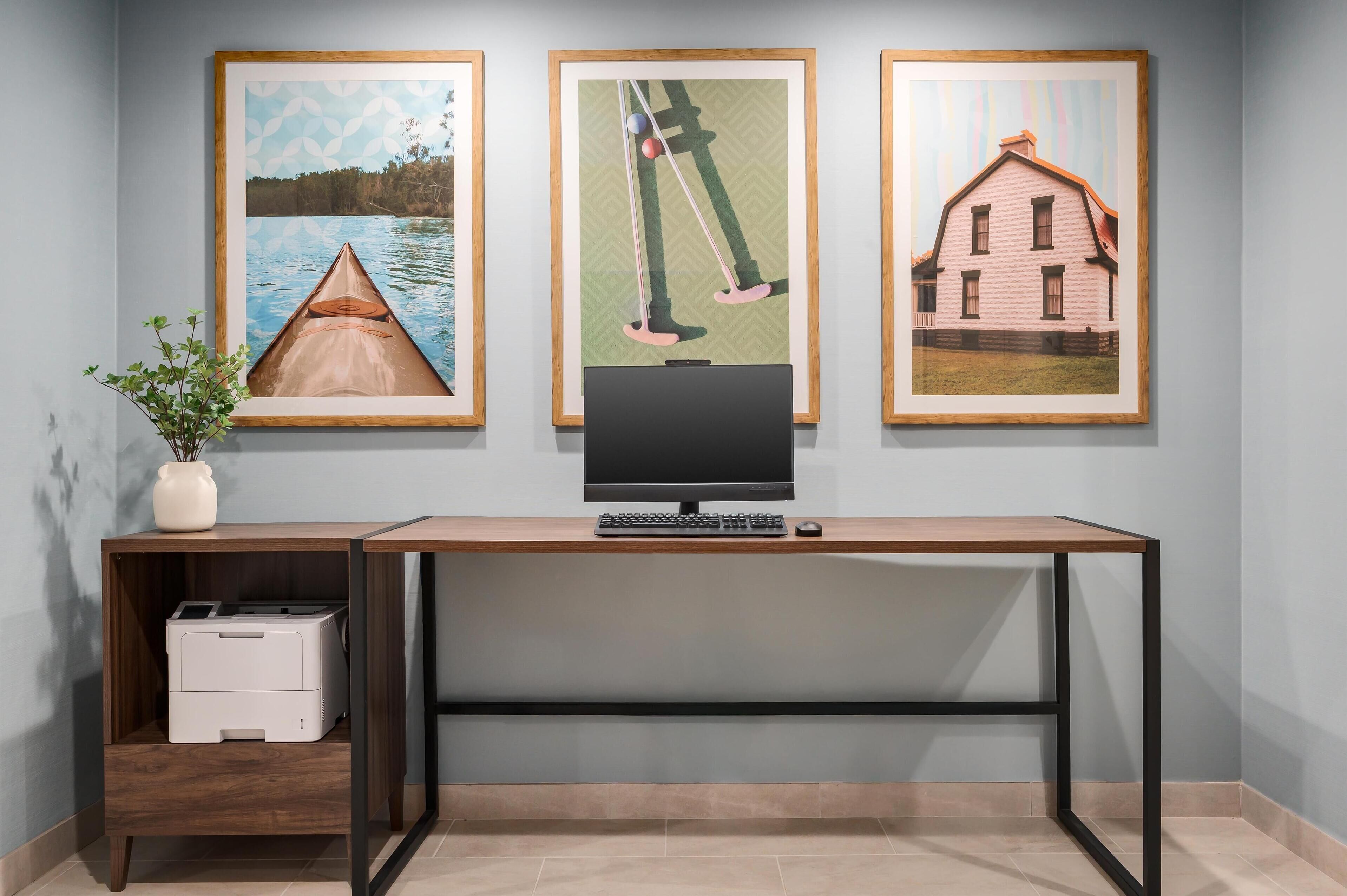 A desk with a computer, framed artwork, and a printer.