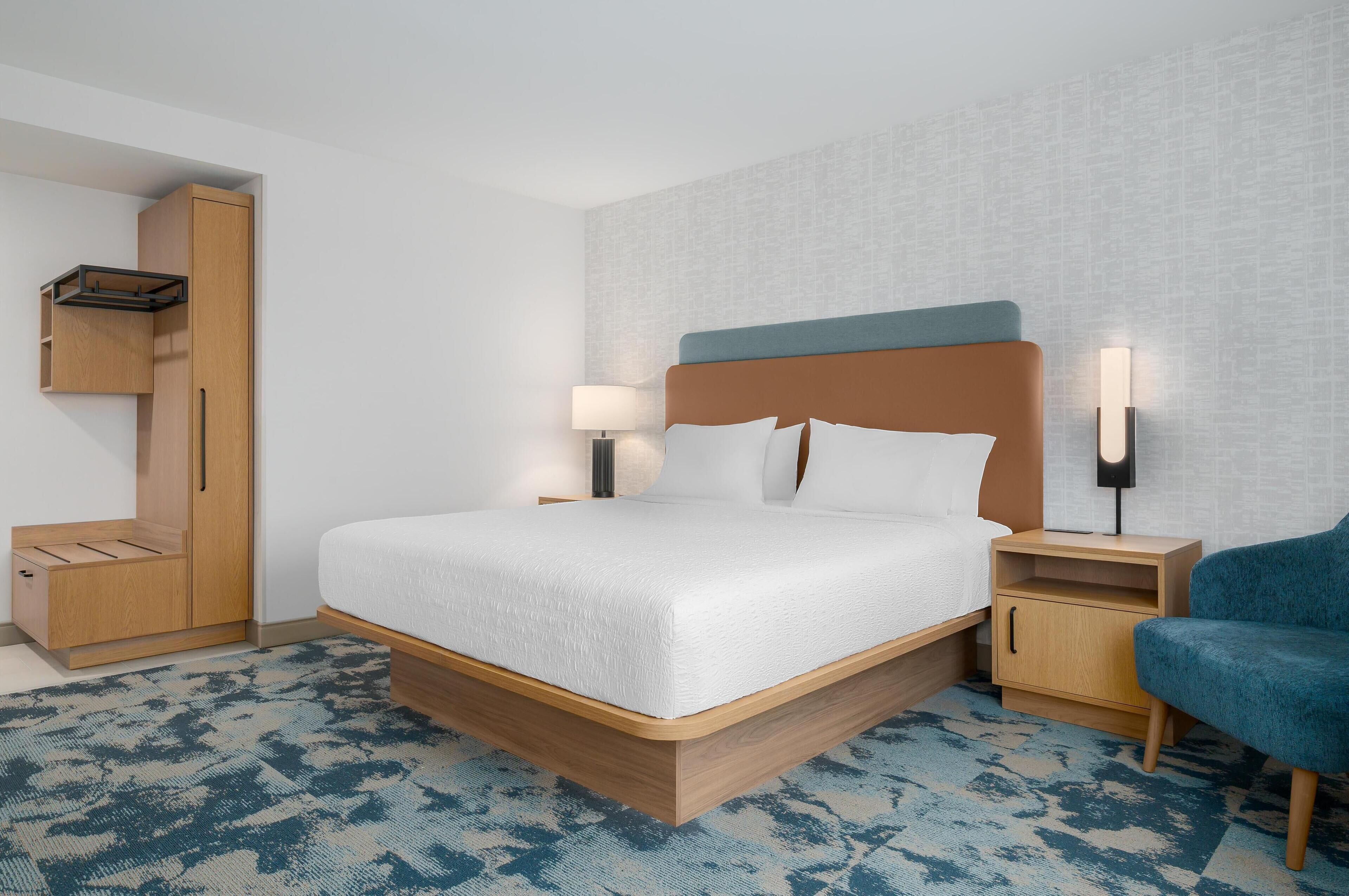 Una habitación de hotel moderna con una cama grande, un armario, una mesita de noche y una silla.