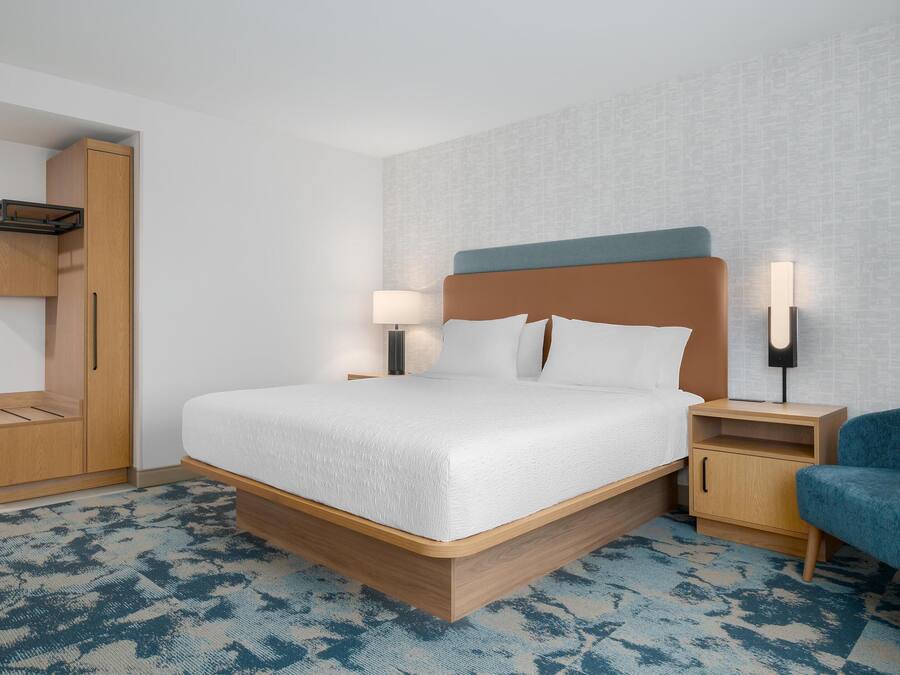 Una habitación de hotel moderna con una cama grande, un armario, una mesita de noche y una silla.