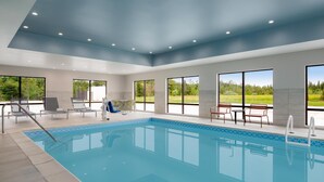 Une piscine intérieure moderne, avec une vue dégagée sur l’extérieur, un sol carrelé et un plafond doté d’un éclairage encastré.