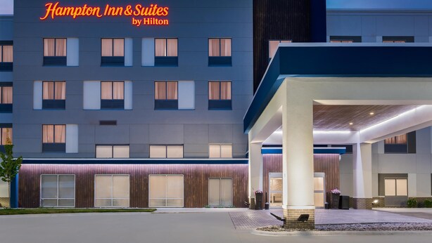 L’extérieur d’un hôtel moderne, avec une enseigne bien visible indiquant « Hampton Inn & Suites by Hilton ».