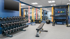 Une salle de sport équipée de supports à poids, d’haltères, d’un banc et d’autres appareils d’exercice.
