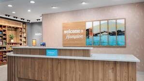 Un hall d'hôtel avec un comptoir d'accueil en bois, une pancarte indiquant « Bienvenue à l'hôtel Hampton » et une vue sur un pont enjambant une étendue d'eau.