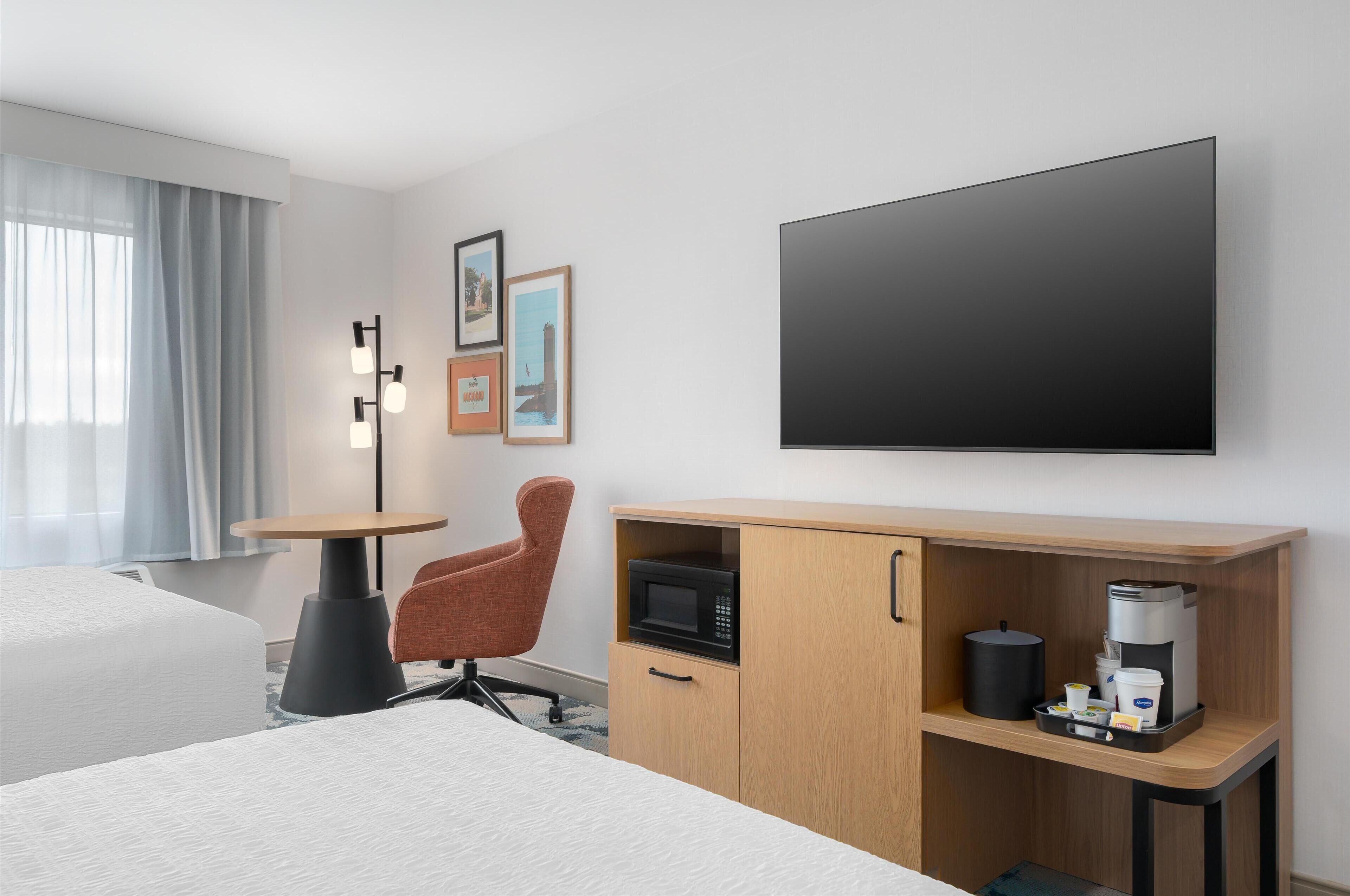 Une chambre d’hôtel avec un lit, un bureau doté d’un micro-ondes, d’une machine à café et d’un téléviseur fixé au mur.
