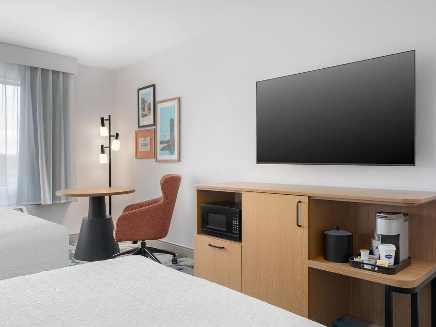 Une chambre d’hôtel avec un lit, un bureau doté d’un micro-ondes, d’une machine à café et d’un téléviseur fixé au mur.