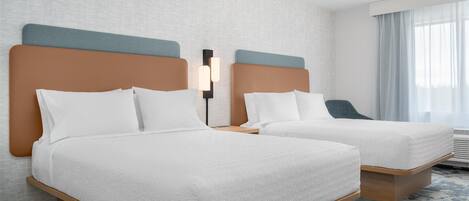 A hotel room with two beds, a nightstand, a lamp, and a window with curtains.