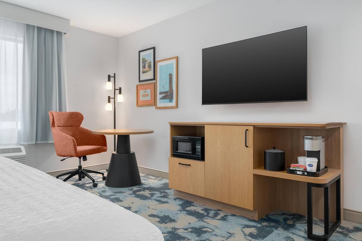 Ett hotellrum med en säng, ett skrivbord med en mikrovågsugn, en kaffebryggare och en stol.