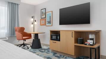 A hotel room with a bed, a desk with a microwave, a coffee maker, and a chair.