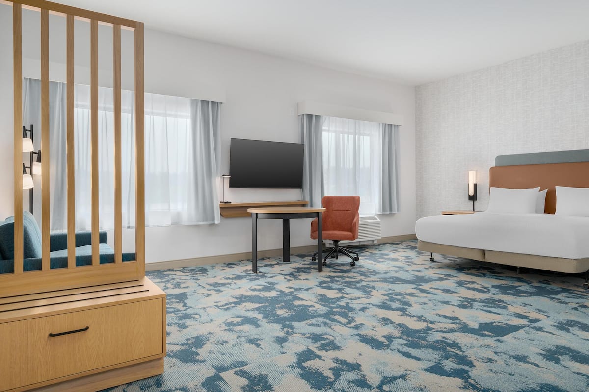 Ett hotellrum med en säng, ett skrivbord med en stol, en tv och ett träskåp.