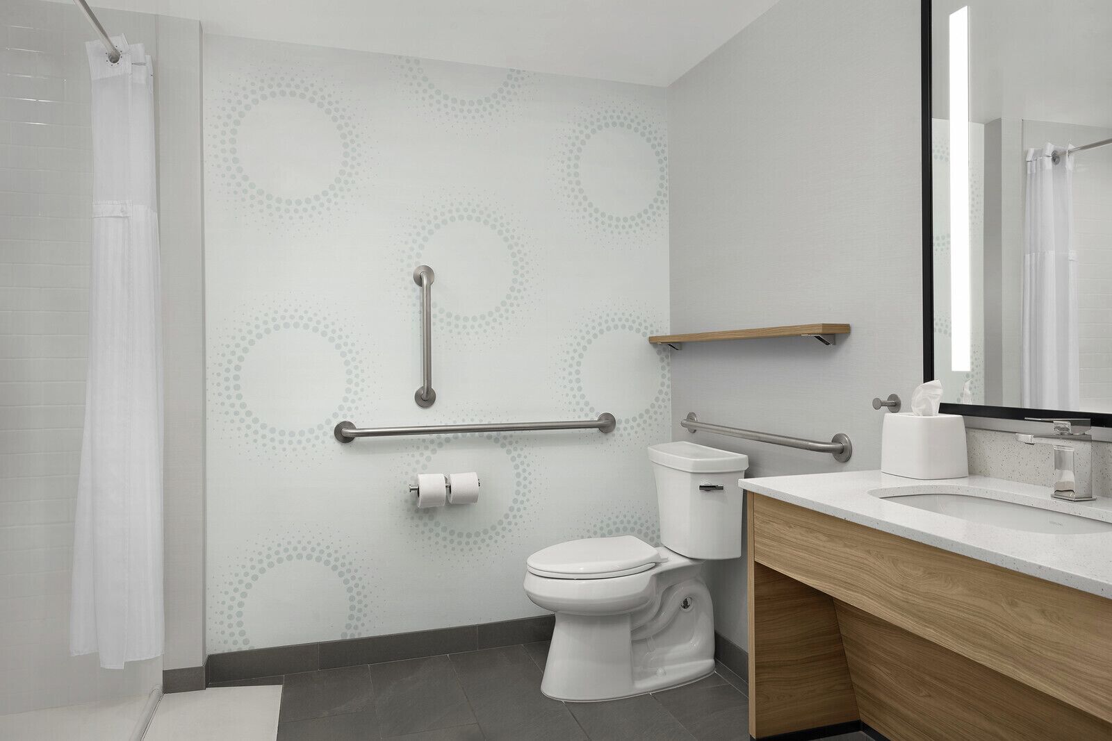 Un bany modern amb vàter, barres de sujeció, cortina de bany i un lavabo amb mirall.