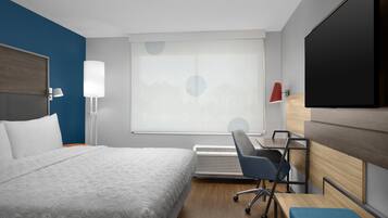 A hotel room with a bed, a desk, a chair, a TV, and a window with blinds.