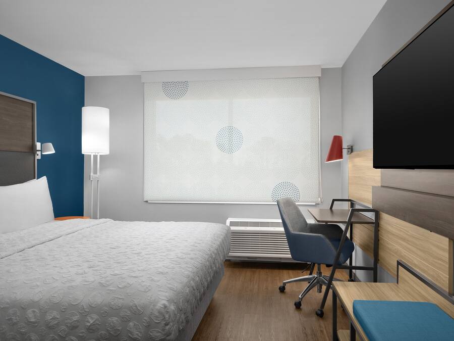 A hotel room with a bed, a desk, a chair, a TV, and a window with blinds.