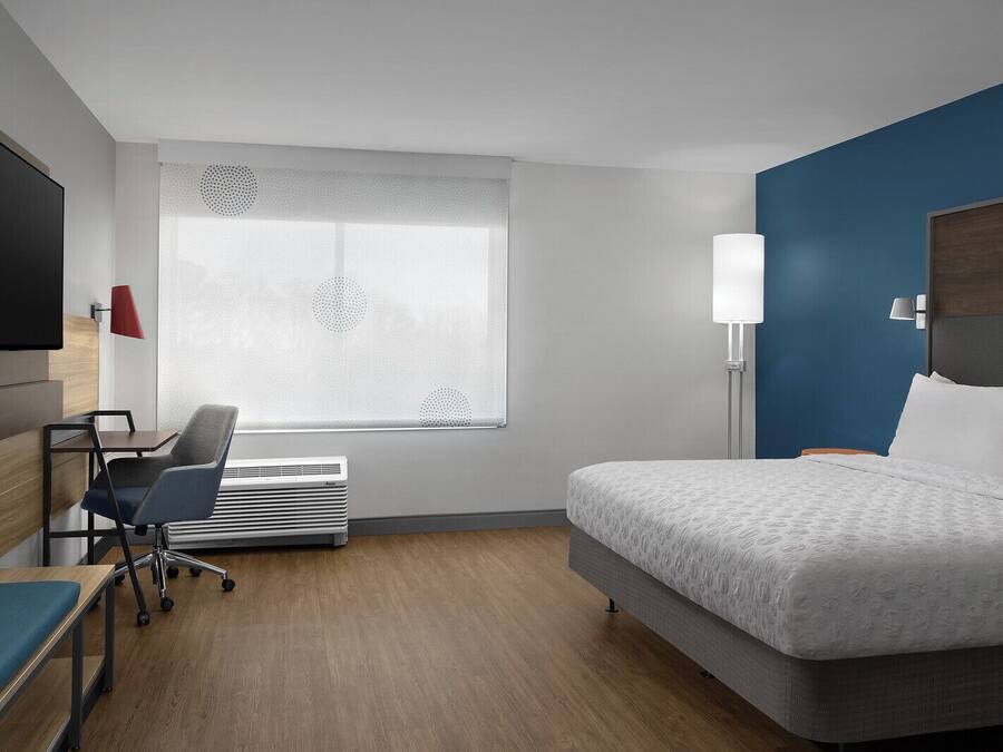 Une chambre d’hôtel comprenant un lit, un bureau avec une chaise, une télévision et une fenêtre ornée d’un motif décoratif.