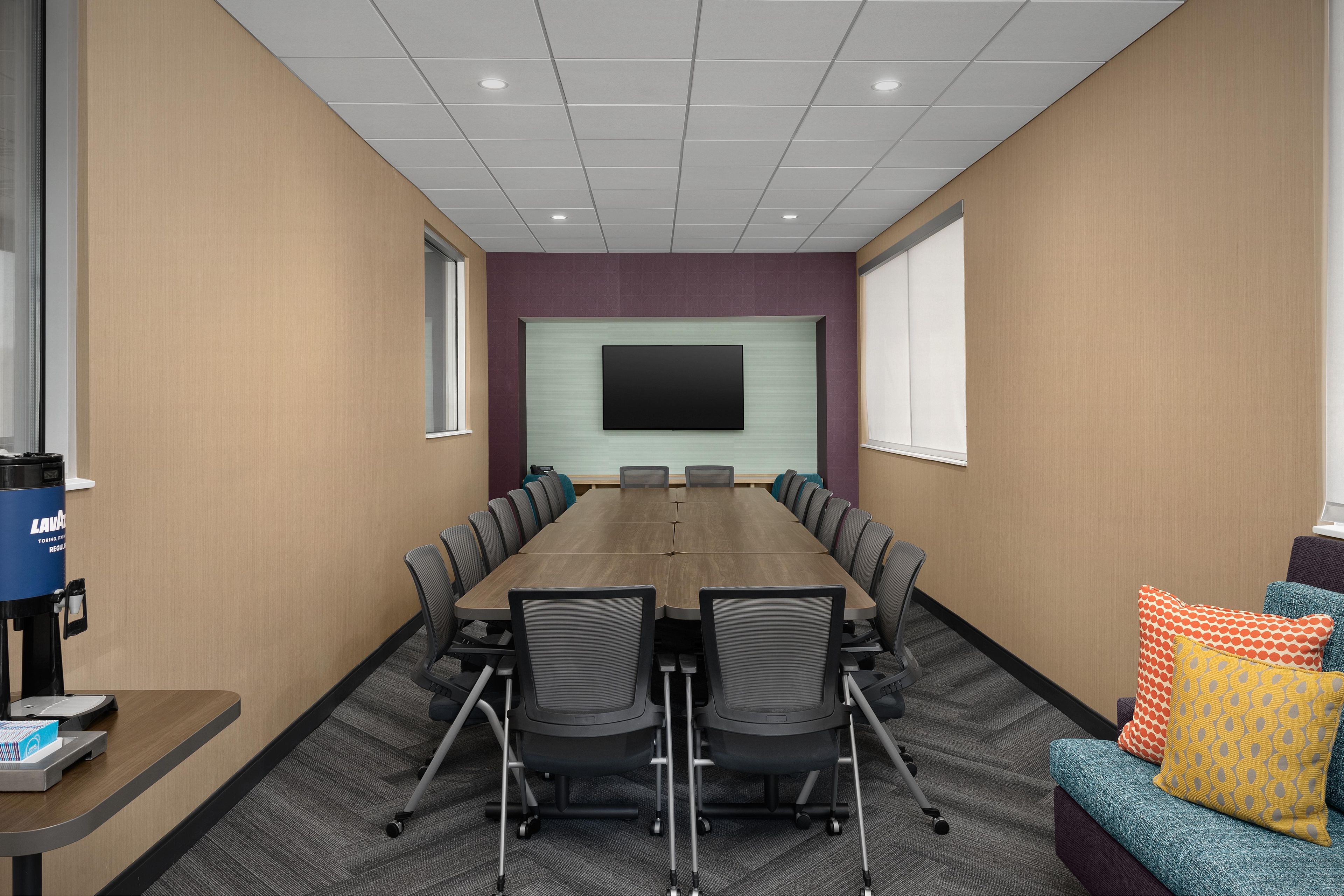 A conference room with a long table, chairs, a TV screen, and a sofa with cushions.