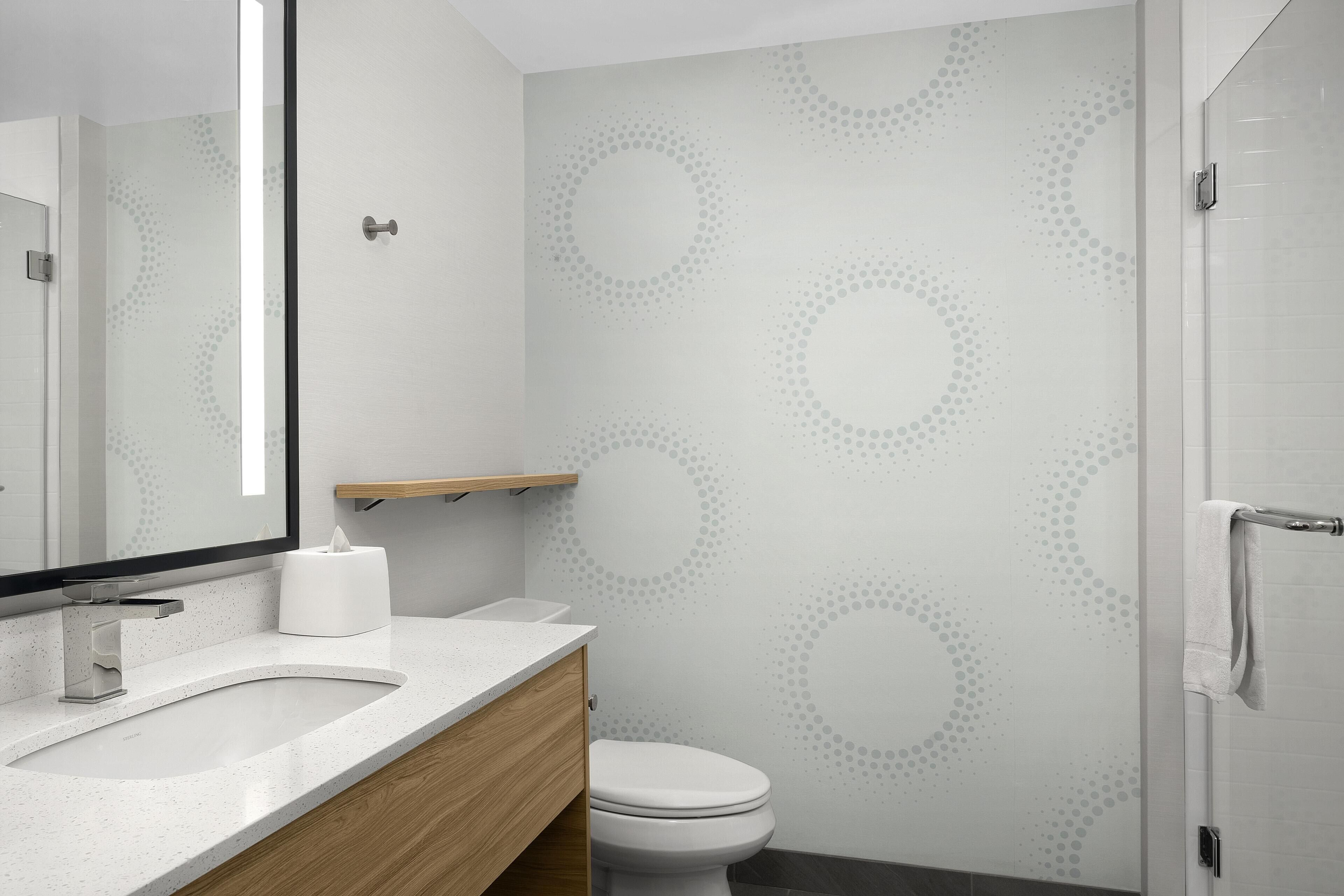 Een moderne badkamer met een wit wastafelmeubel, spiegel en toilet. Er is een handdoekhouder aan de muur en een toiletpapierrolhouder op het aanrecht.