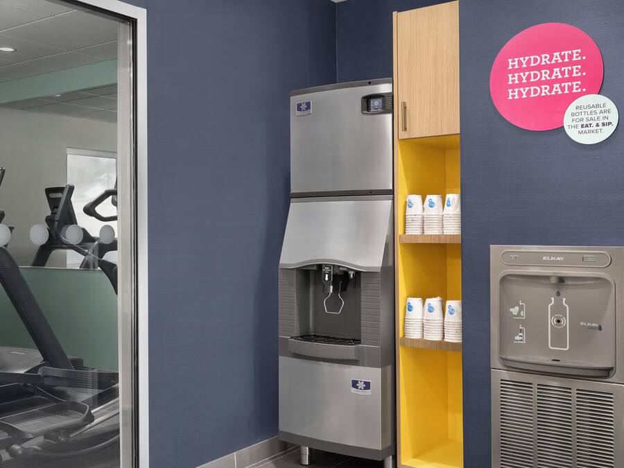 Un espacio de acondicionamiento físico con equipo de ejercicio, un dispensador de agua y una pared con recordatorios de hidratación.