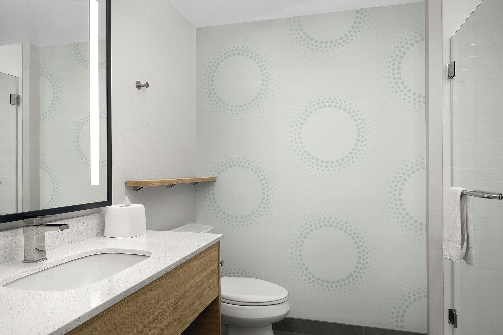 A modern bathroom with a white sink, wooden vanity, a toilet, and a shower area.