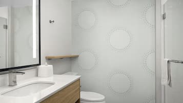 A modern bathroom with a white sink, wooden vanity, a toilet, and a shower area.