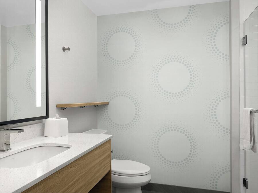 A modern bathroom with a white sink, wooden vanity, a toilet, and a shower area.