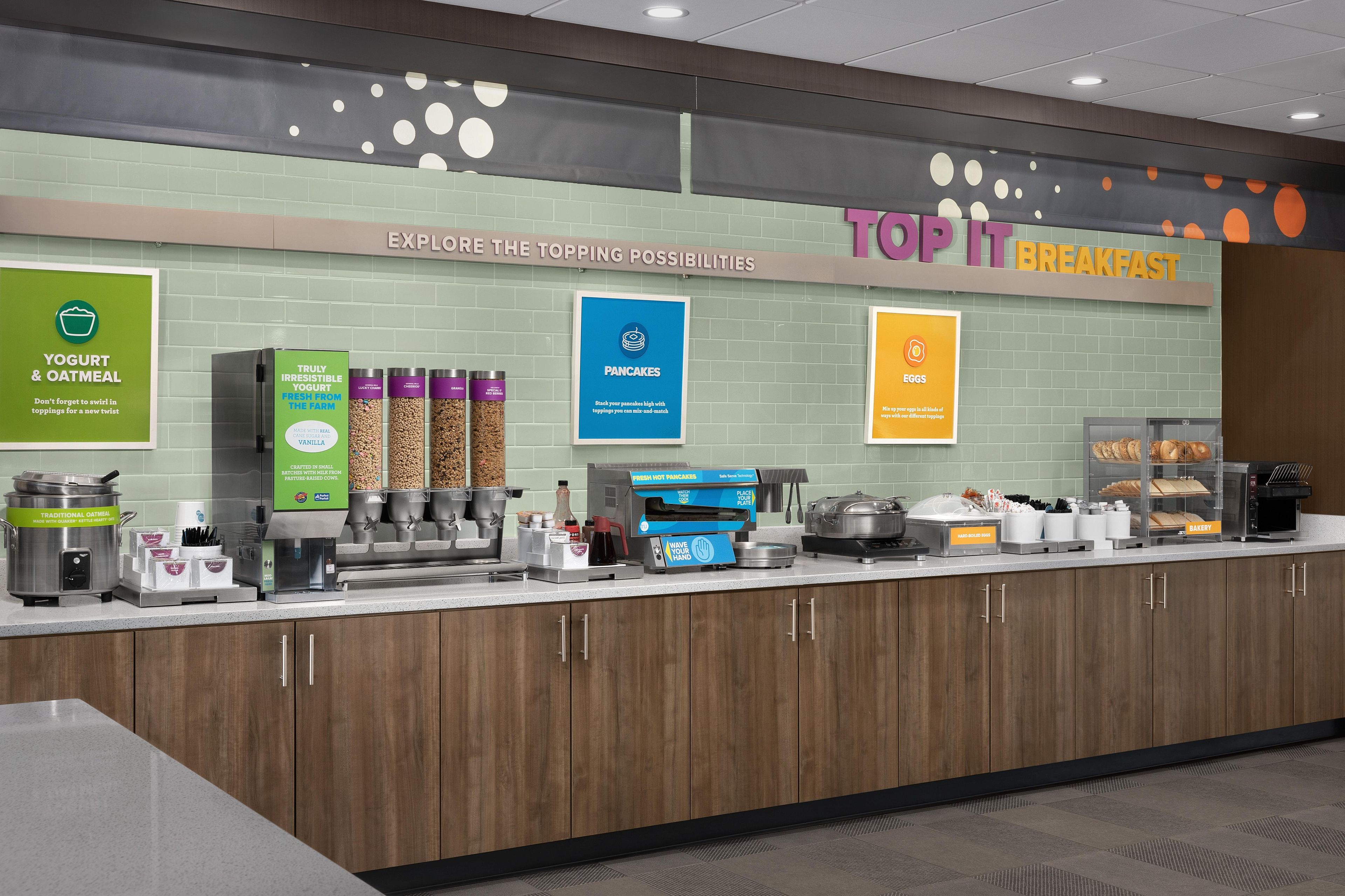 A breakfast buffet area with yogurt, oatmeal, pancakes, eggs, and bakery items.