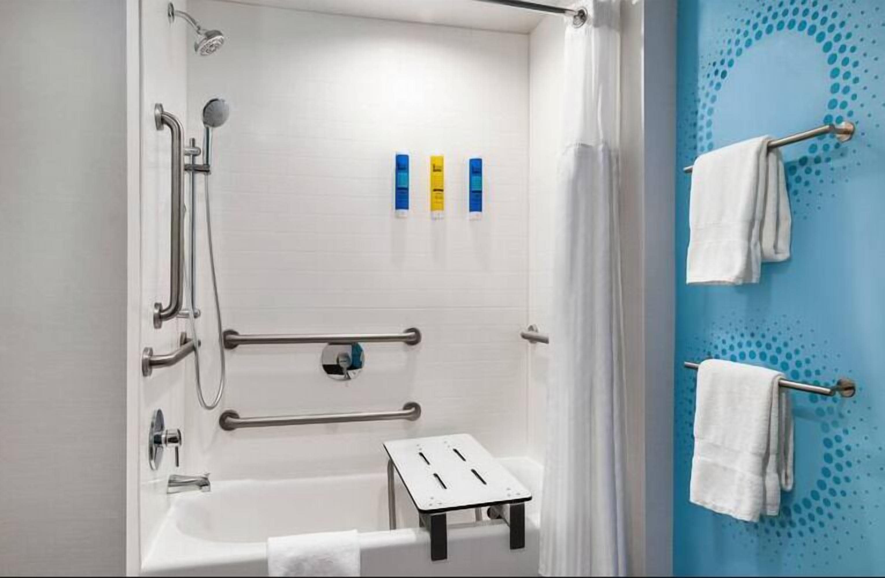 A bathroom with a bathtub, grab bars, a showerhead, and a towel rack.