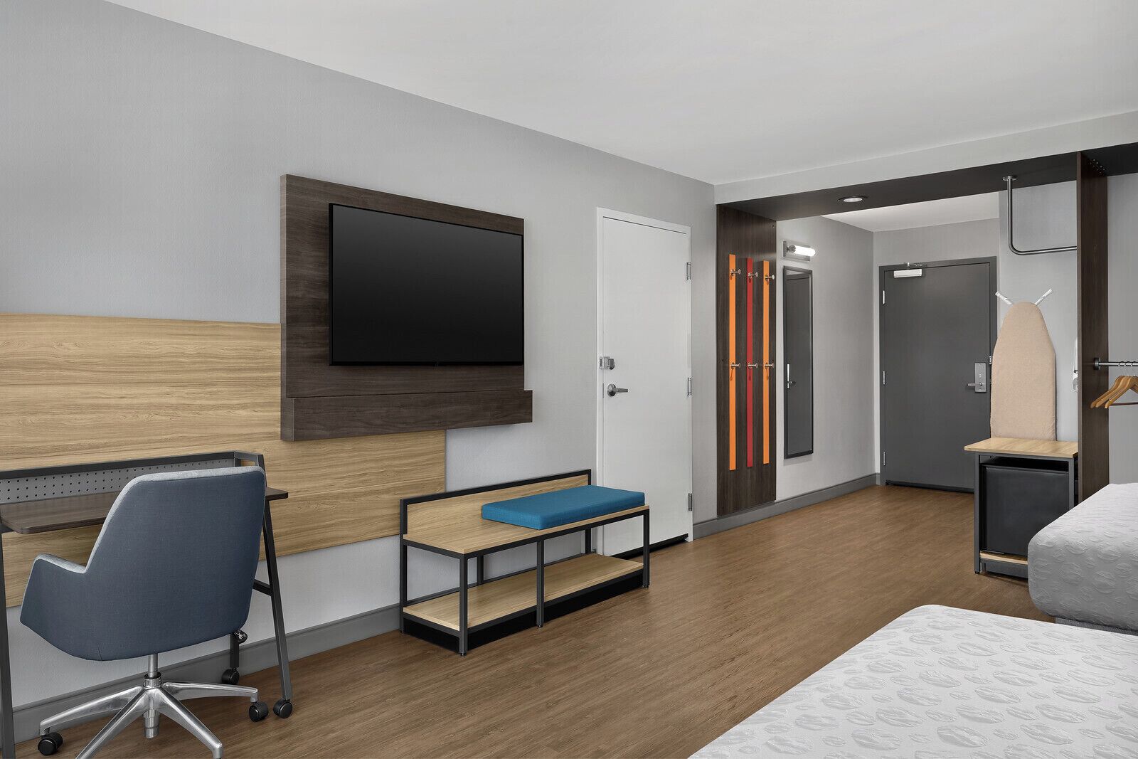 Et moderne hotelværelse med sengegavl i træ, et fladskærms-tv, et skrivebord med stol, en bænk, en seng og et klædeskab.
