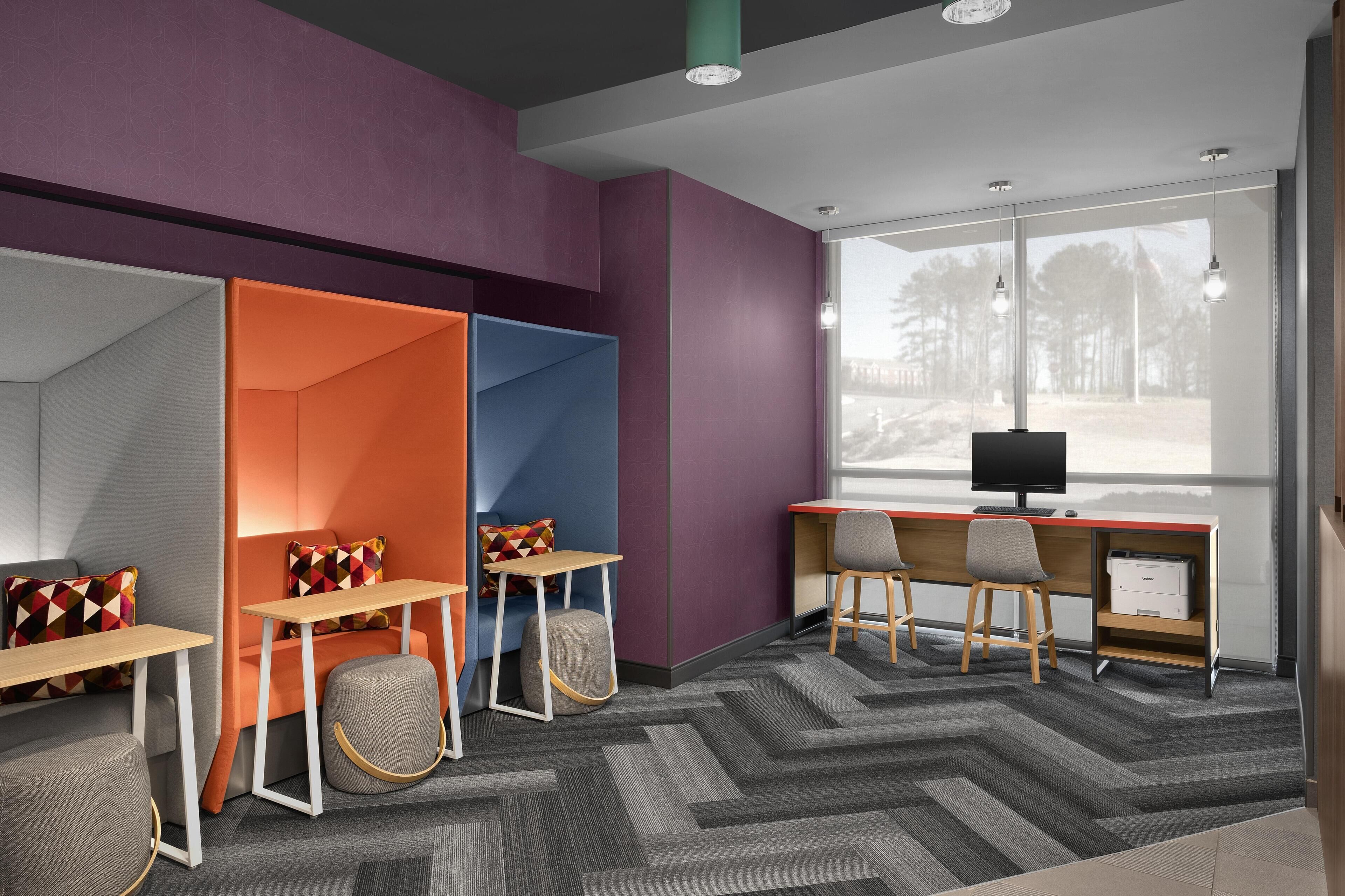 A modern office space with a large desk, two chairs, a computer, and a window with a view of trees.