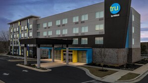 Un edificio de hotel moderno con un llamativo letrero 'tru by Hilton', varios pisos y una zona de acceso cubierta.