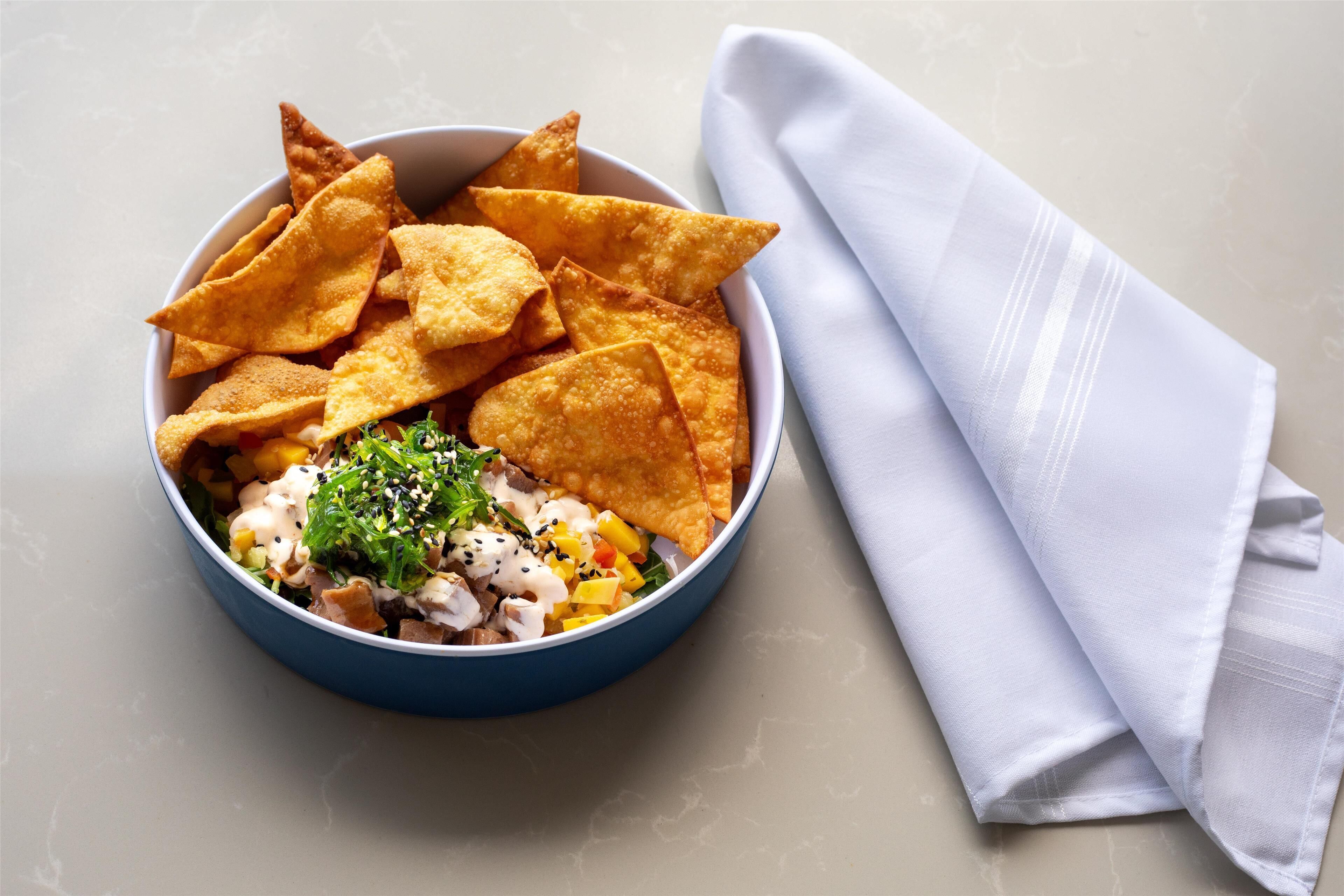 A bowl of food with chips and a napkin on a table.