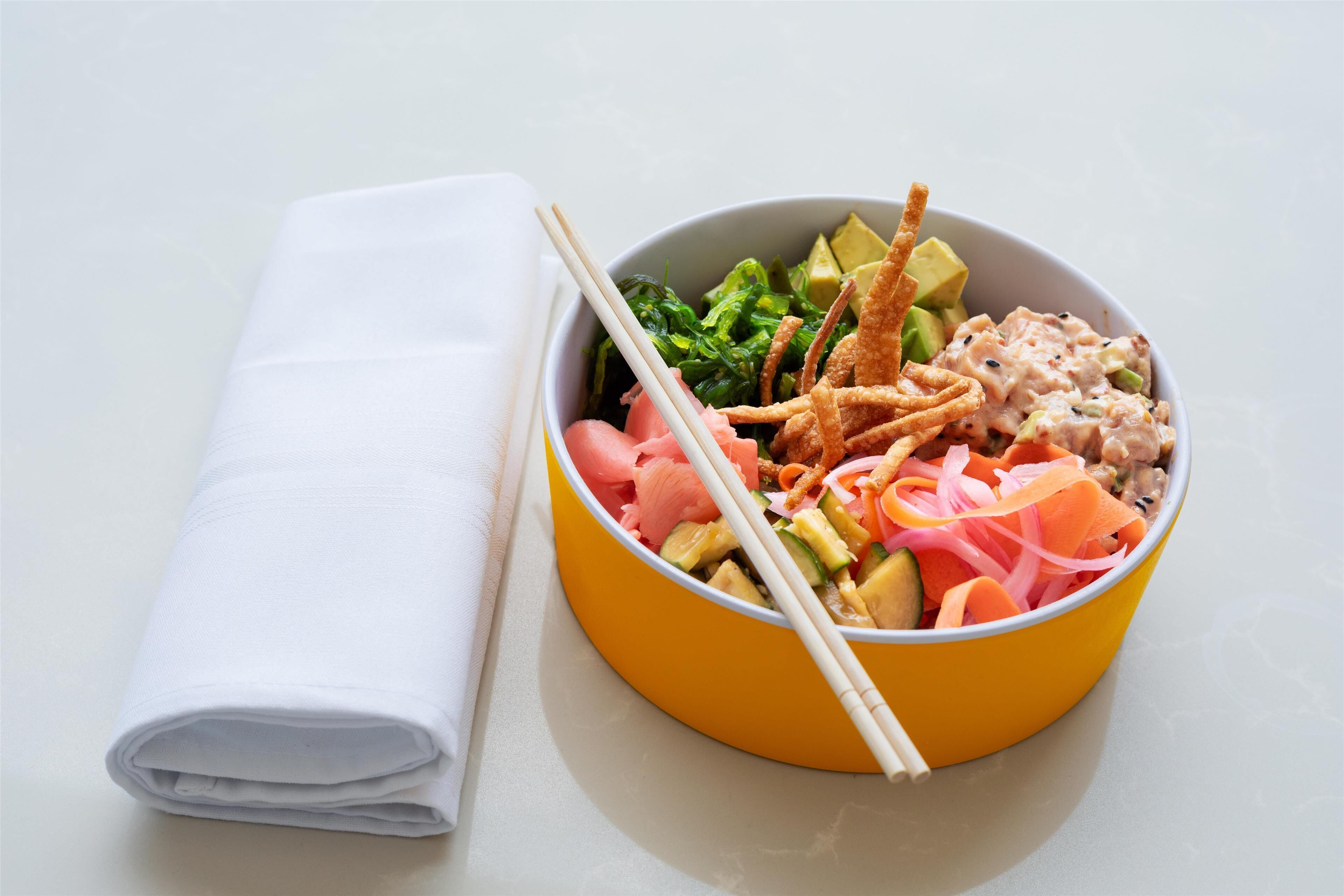 A bowl of food with chopsticks and a folded napkin on a table.