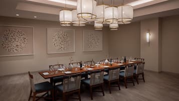 Uma sala de jantar com uma longa mesa de madeira posta para seis pessoas, cercada por cadeiras de vime. Há três grandes peças de arte circular nas paredes acima da mesa.