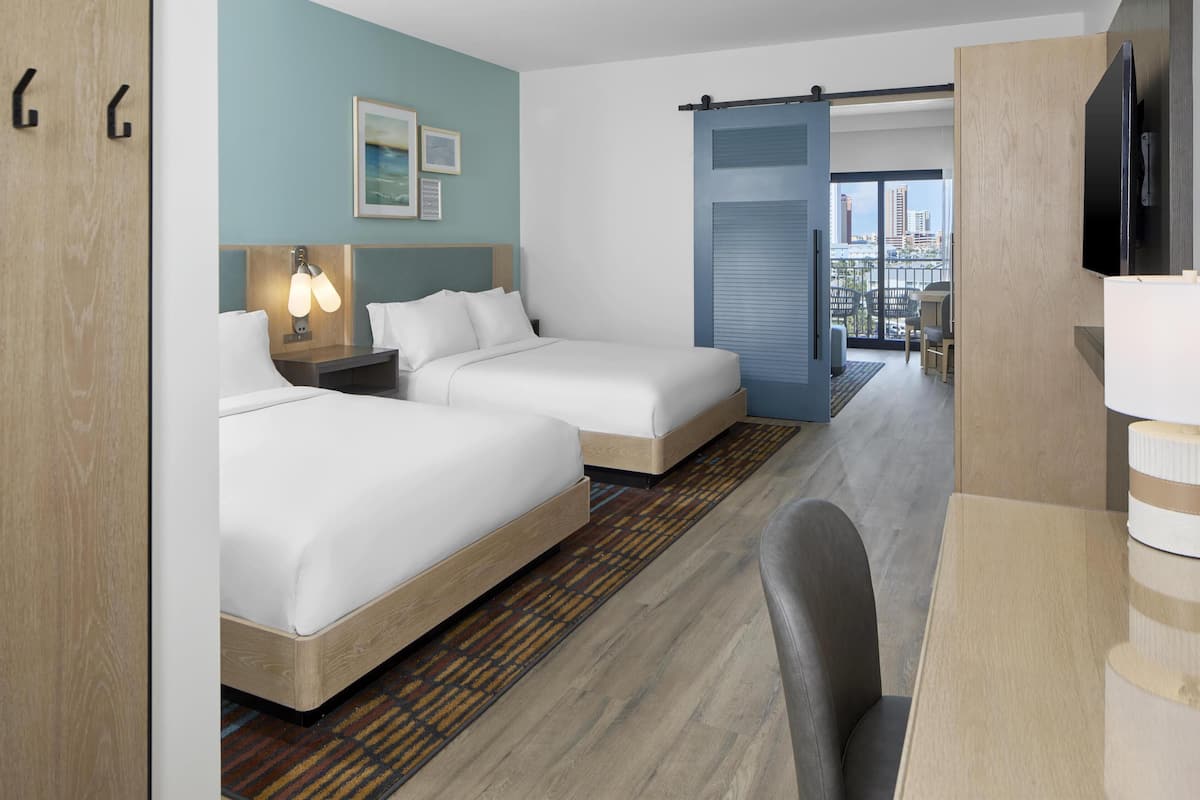 Ein Hotelzimmer mit zwei Betten, einem Schreibtisch, einem Stuhl, einem Fernseher und Blick auf die Stadt.
