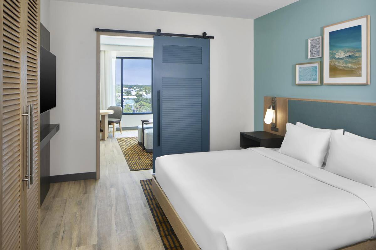 Ein Hotelzimmer mit Bett, Fernseher, Schreibtisch, Stuhl, Balkon und Blick ins Freie.
