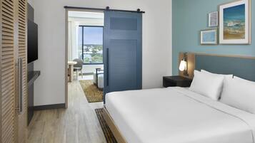 A hotel room with a bed, a TV, a desk, a chair, a balcony, and a view of the outdoors.