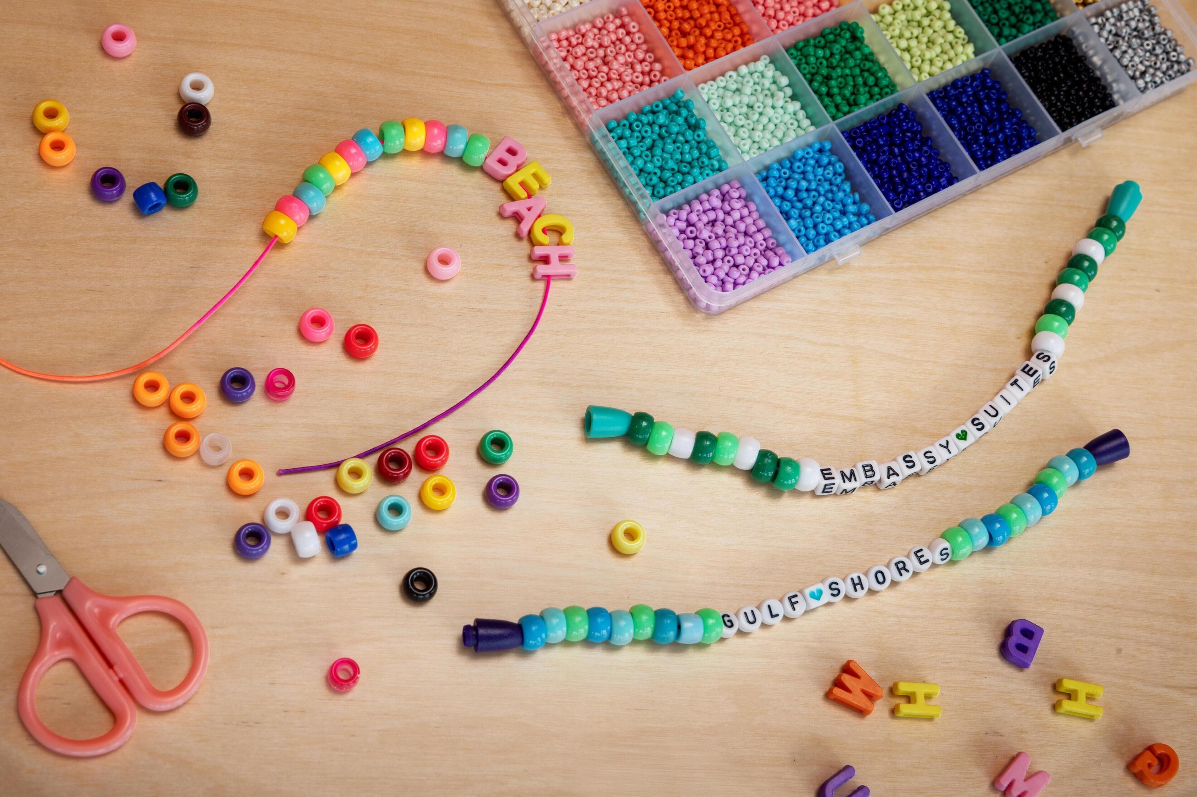 A workspace with beads, letters, and a pair of scissors on a wooden surface.