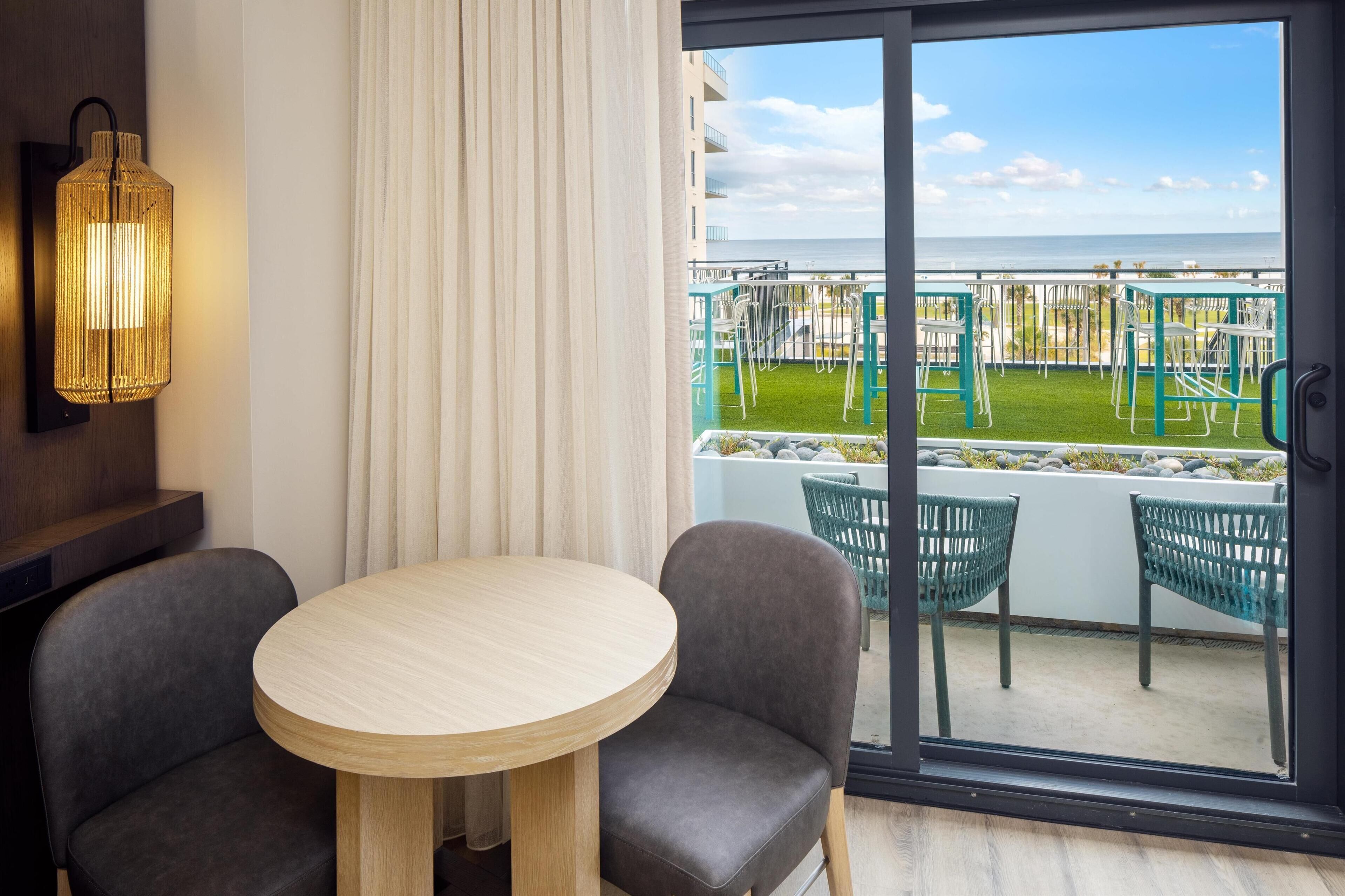 Un balcon avec vue sur la mer, une table ronde avec deux chaises et un luminaire fixé au mur.