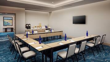 A conference room with a long table, chairs, a coffee station, and a TV on the wall.